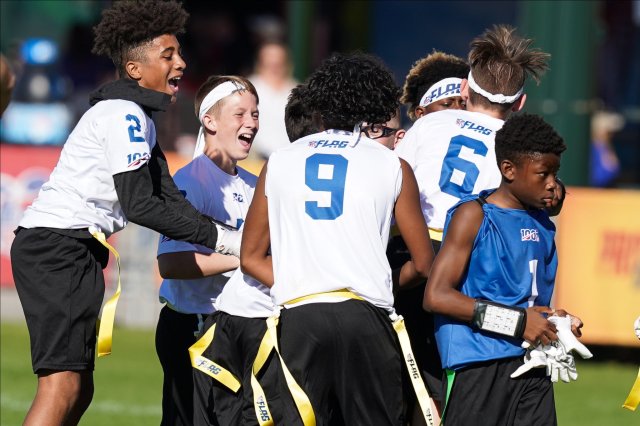 NFL FLAG group of boys celebrating in a huddle. White jerseys with blue lettering.